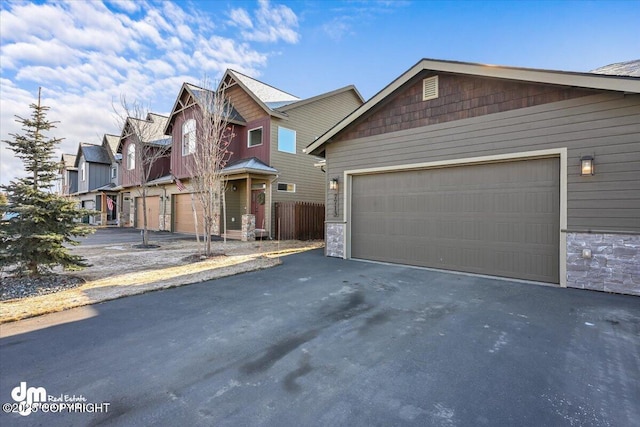 view of front facade featuring aphalt driveway, a residential view, a garage, and stone siding