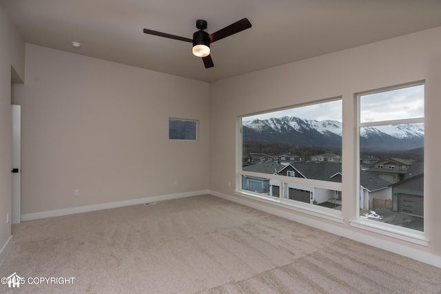 spare room featuring carpet, a mountain view, baseboards, and ceiling fan