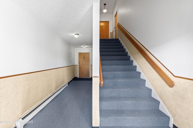 stairway with a wainscoted wall, a baseboard radiator, and a textured ceiling