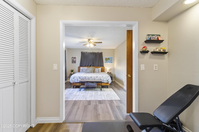 bedroom with a closet, a ceiling fan, a textured ceiling, wood finished floors, and baseboards