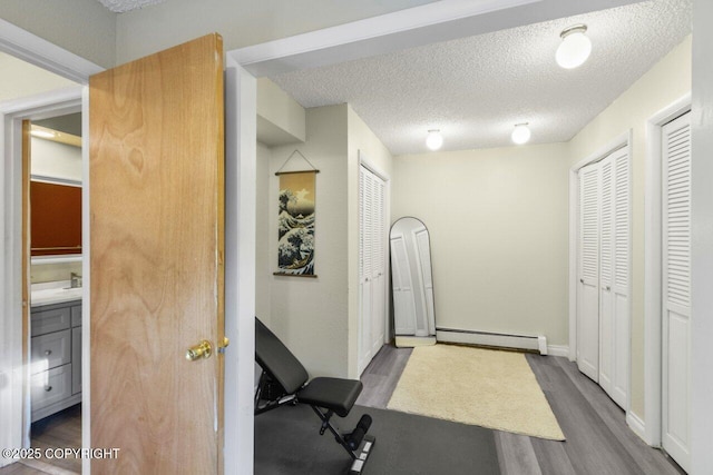 exercise room featuring baseboards, a textured ceiling, a baseboard heating unit, and wood finished floors