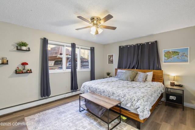 bedroom featuring ceiling fan, a textured ceiling, a baseboard heating unit, wood finished floors, and baseboards