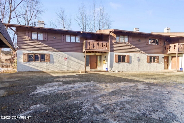 rear view of house featuring a balcony, a chimney, and stucco siding