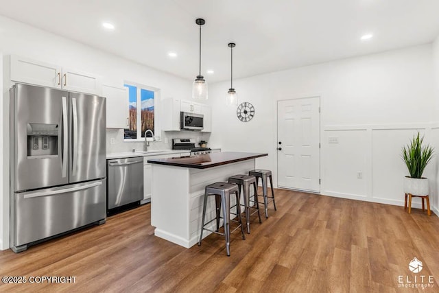 kitchen with a breakfast bar area, a center island, stainless steel appliances, white cabinetry, and a sink