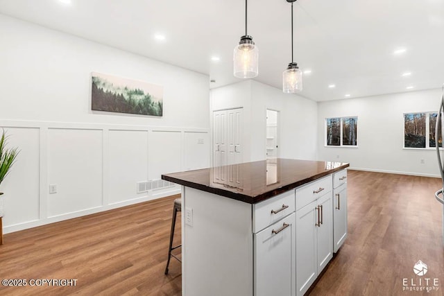 kitchen featuring a breakfast bar, visible vents, a decorative wall, and wood finished floors