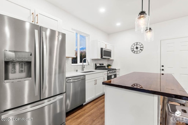 kitchen with light wood-style flooring, appliances with stainless steel finishes, a sink, white cabinetry, and backsplash