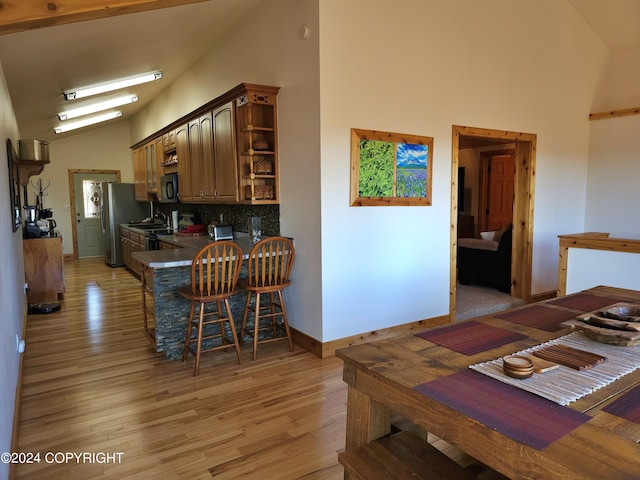 kitchen featuring dark countertops, a breakfast bar, light wood-type flooring, high vaulted ceiling, and open shelves