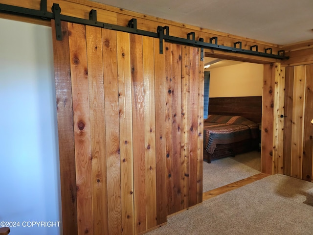 hall featuring a barn door, wood walls, and carpet flooring