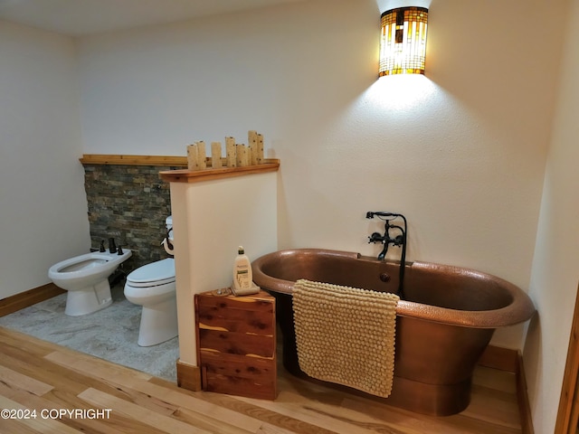 full bathroom featuring toilet, wood finished floors, baseboards, a freestanding bath, and a bidet