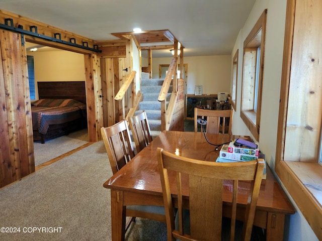 carpeted dining room with a barn door and stairs