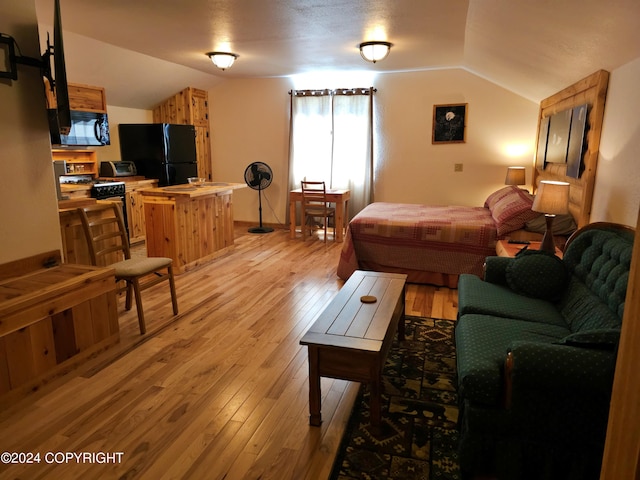 bedroom with lofted ceiling, light wood-style flooring, freestanding refrigerator, and a toaster