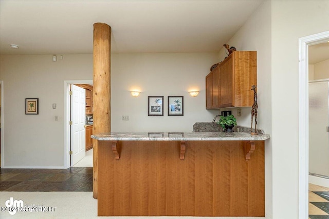 kitchen featuring light stone counters, a peninsula, a kitchen breakfast bar, baseboards, and brown cabinets