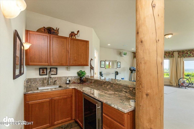 kitchen featuring beverage cooler, brown cabinets, a sink, and stone countertops