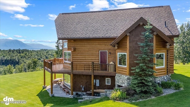 back of property with roof with shingles, a yard, a patio, a deck with mountain view, and log siding