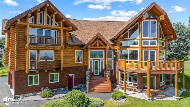 back of house with a shingled roof, a patio area, and log exterior