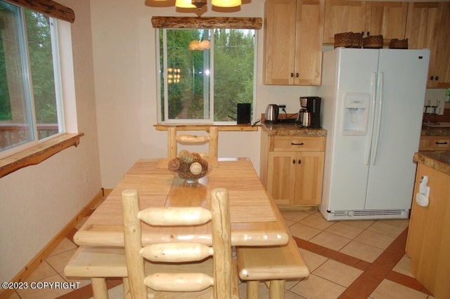 kitchen featuring white fridge with ice dispenser, light brown cabinetry, baseboards, and light tile patterned floors