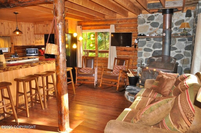 living room with a wood stove, beamed ceiling, and wood finished floors