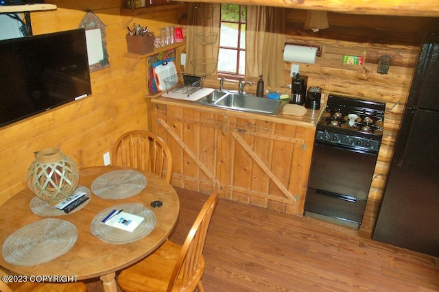 kitchen featuring rustic walls, black appliances, a sink, and wood finished floors