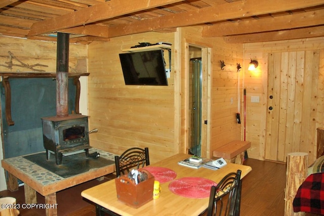 dining area featuring wooden ceiling, wood walls, wood finished floors, beamed ceiling, and a wood stove