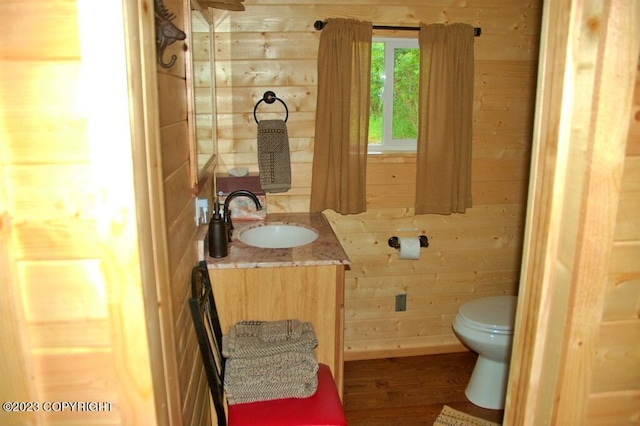 bathroom with toilet, wood walls, wood finished floors, and vanity