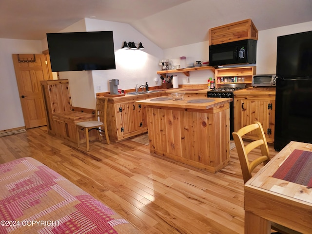 kitchen with lofted ceiling, a sink, butcher block countertops, light wood-type flooring, and black appliances