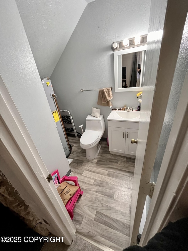 half bathroom featuring a textured wall, toilet, wood finished floors, vanity, and vaulted ceiling