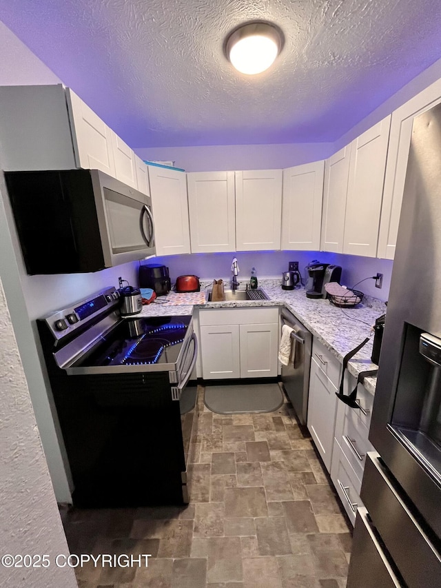 kitchen featuring stainless steel appliances, a sink, white cabinets, light stone countertops, and stone finish floor