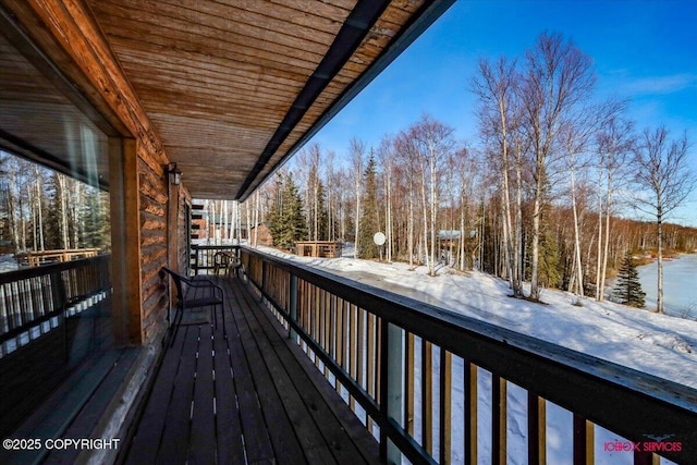 snow covered deck featuring a view of trees