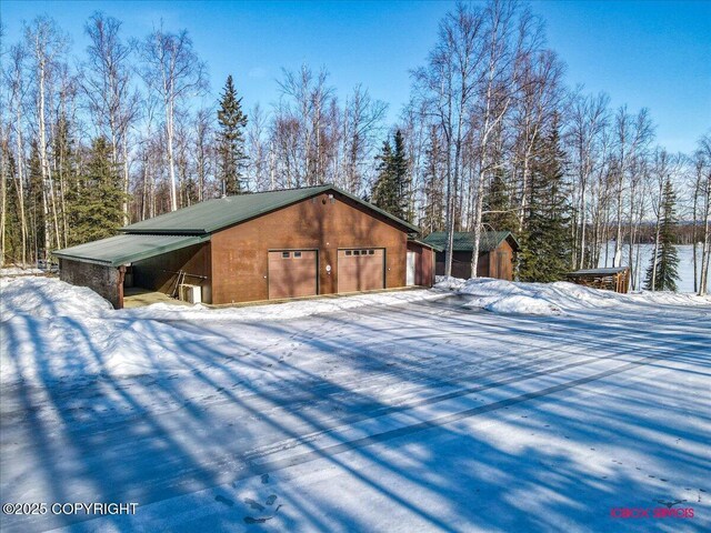 view of snowy exterior featuring an outbuilding, metal roof, and a detached garage