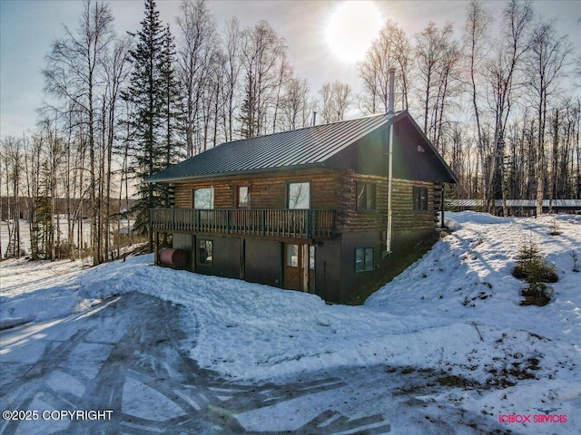 snow covered back of property featuring a standing seam roof, a wooden deck, log exterior, and metal roof