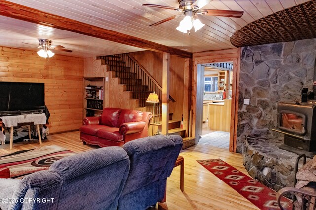 living area featuring a ceiling fan, wood finished floors, a wood stove, stairs, and wood walls