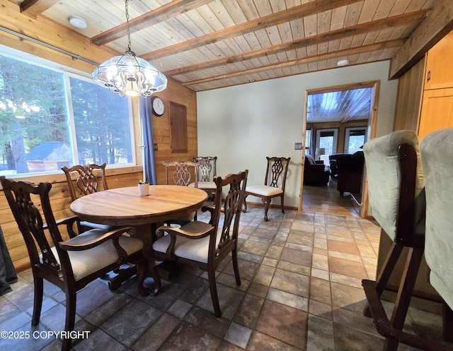 dining room with beamed ceiling, a notable chandelier, stone tile flooring, wooden walls, and wood ceiling