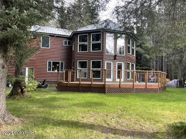 rear view of house featuring a lawn, a wooden deck, log veneer siding, and metal roof