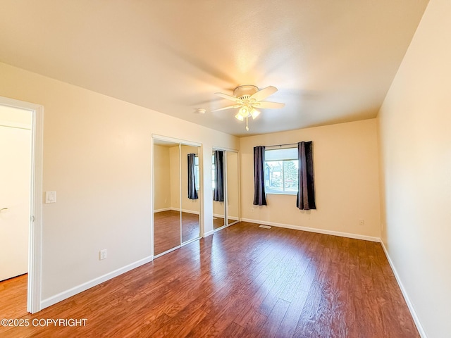 unfurnished bedroom with baseboards, two closets, wood finished floors, and a ceiling fan