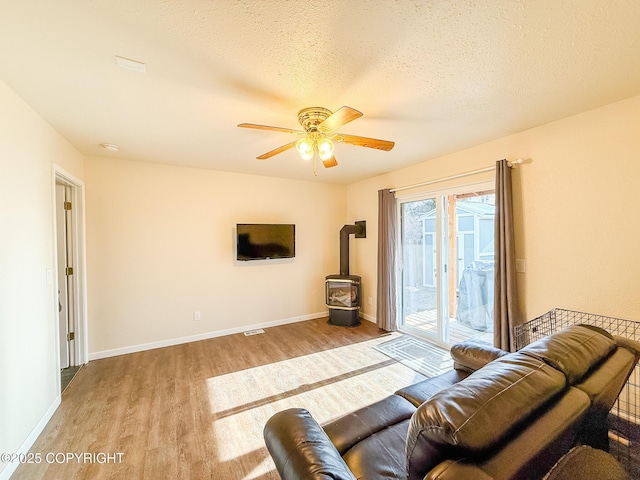 living room with baseboards, ceiling fan, a wood stove, wood finished floors, and a textured ceiling