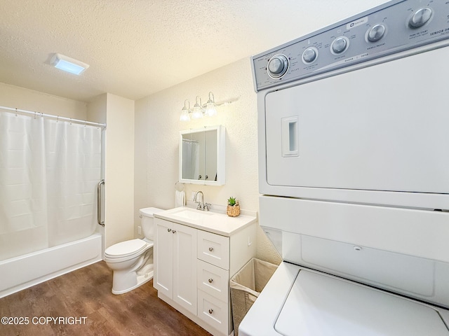 bathroom featuring toilet, stacked washer and clothes dryer, a textured ceiling, wood finished floors, and vanity