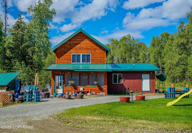 back of house with metal roof, gravel driveway, and a yard