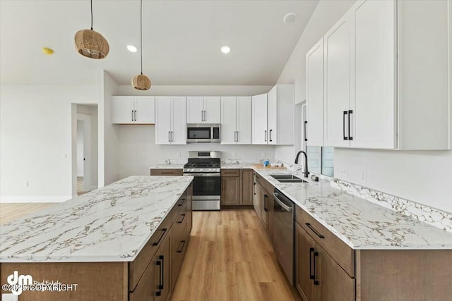 kitchen featuring light wood finished floors, a kitchen island, appliances with stainless steel finishes, white cabinets, and a sink