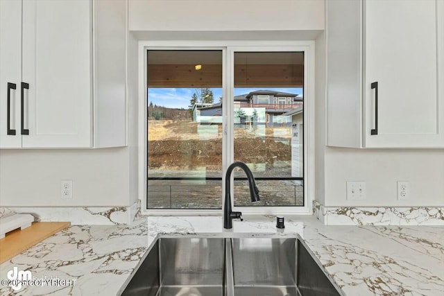 kitchen with a sink, light stone counters, and white cabinets