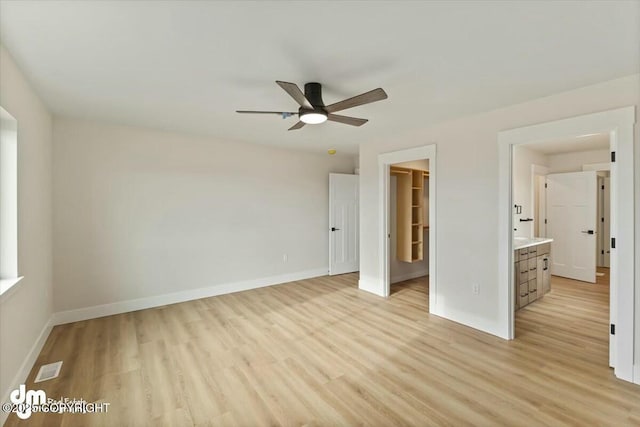 unfurnished bedroom with a ceiling fan, baseboards, light wood-style flooring, a closet, and a walk in closet