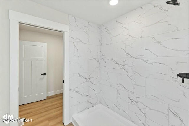 full bath with baseboards, tiled shower, and wood finished floors