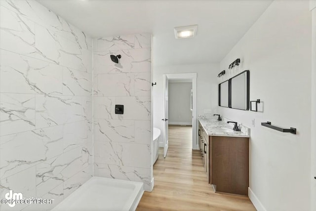 bathroom featuring a tile shower, vanity, baseboards, and wood finished floors