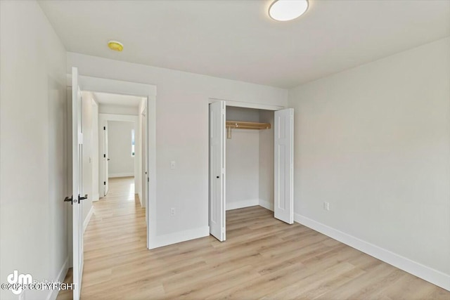 unfurnished bedroom featuring light wood-style flooring, baseboards, and a closet