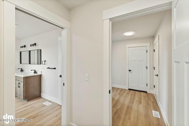 corridor with light wood finished floors, visible vents, and baseboards