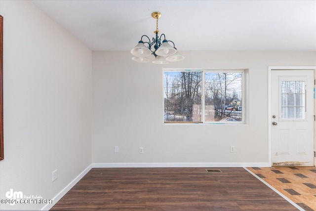 unfurnished dining area featuring visible vents, a notable chandelier, baseboards, and wood finished floors