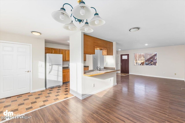 kitchen featuring baseboards, wood finished floors, freestanding refrigerator, and brown cabinets