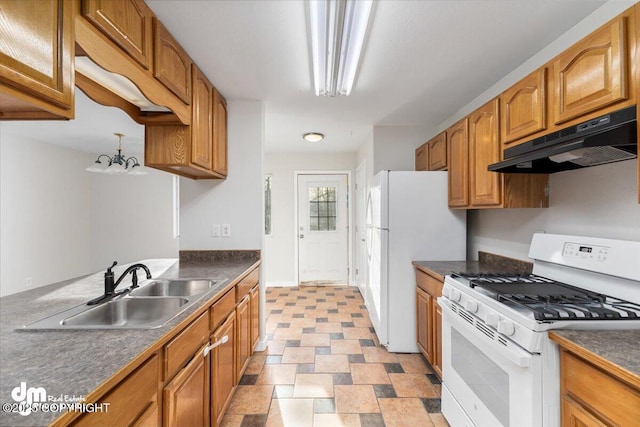 kitchen featuring dark countertops, brown cabinetry, a sink, white appliances, and under cabinet range hood