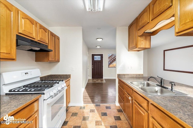 kitchen with dark countertops, white gas stove, under cabinet range hood, and a sink