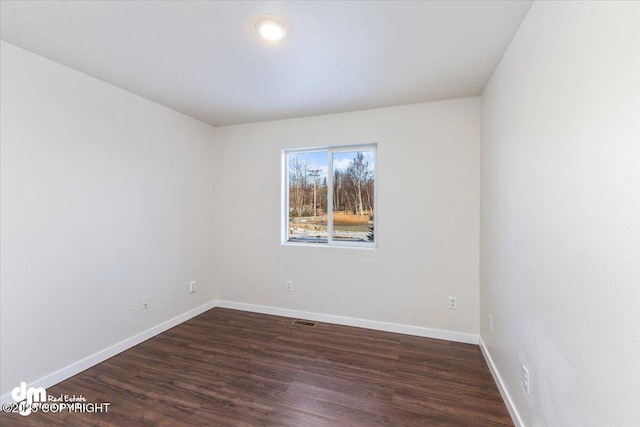 empty room with visible vents, dark wood finished floors, and baseboards