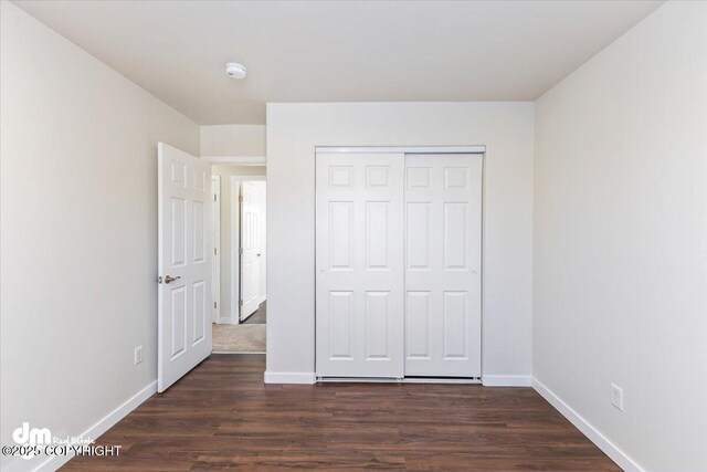 unfurnished bedroom with a closet, baseboards, and dark wood-type flooring